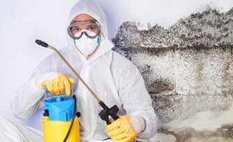 technician in PPE with a pump sprayer disinfectant during remediation.