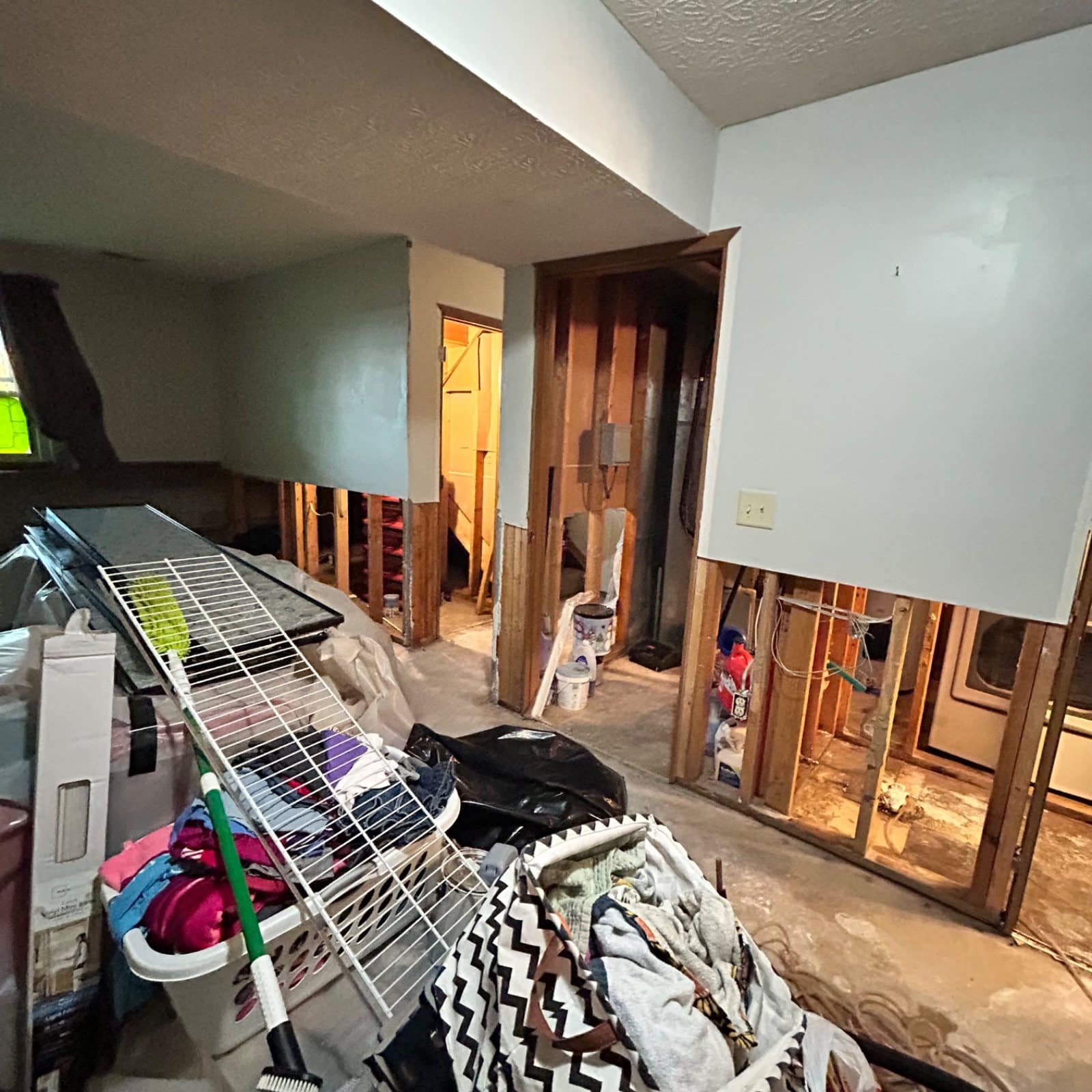 Basement with drywall removed and drying racks deployed during water damage response—clothing and textiles staged for drying