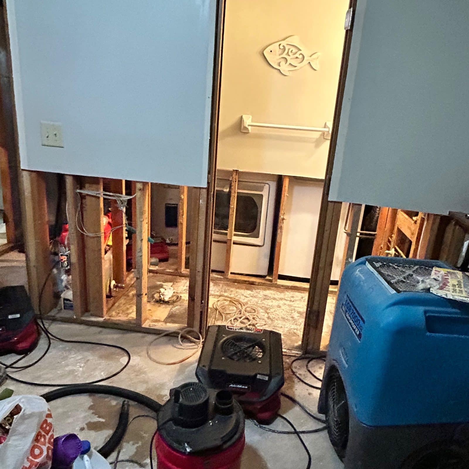 Active water damage drying setup: dehumidifiers and air movers deployed in open wall cavity space during remediation phase
