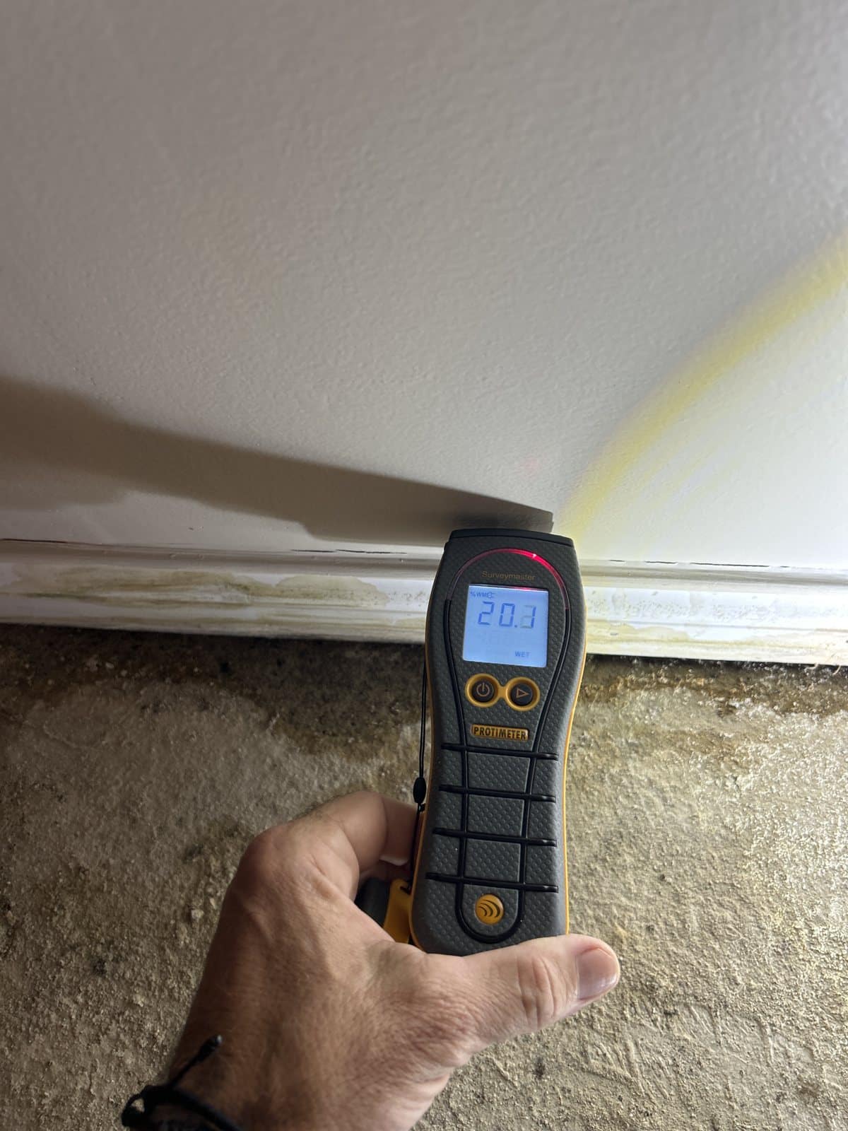 Moisture meter reading 20.1 on stained concrete foundation—visible efflorescence and water damage marks present