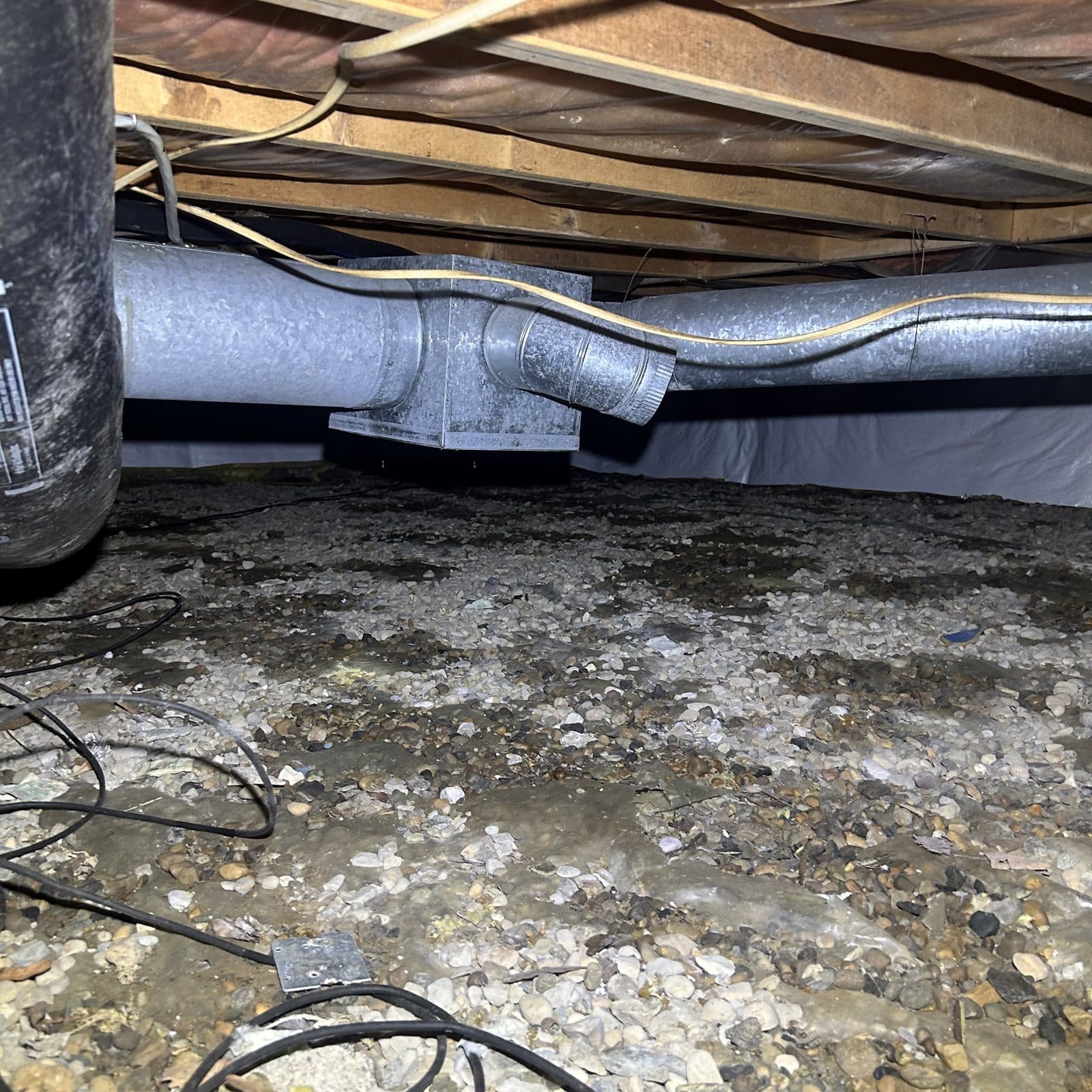 Crawlspace with moisture, gravel base, and containment setup during mold remediation work